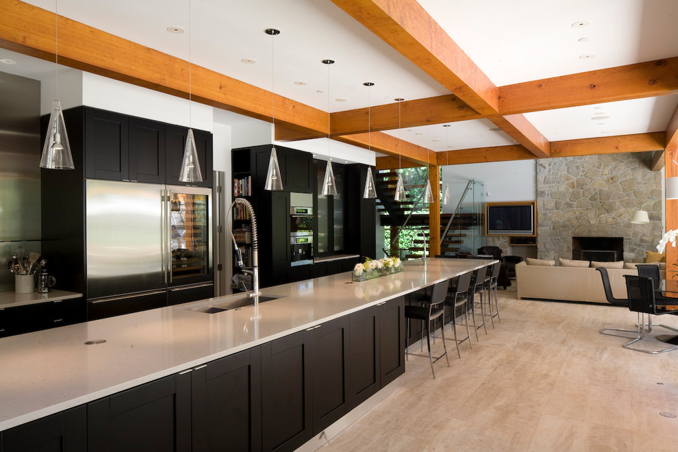 This is an example of a contemporary galley open plan kitchen in Vancouver with shaker cabinets, black cabinets and stainless steel appliances.