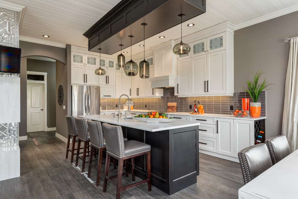 Traditional l-shaped open plan kitchen in Calgary with shaker cabinets, white cabinets, grey splashback, stainless steel appliances, with island and an undermount sink.