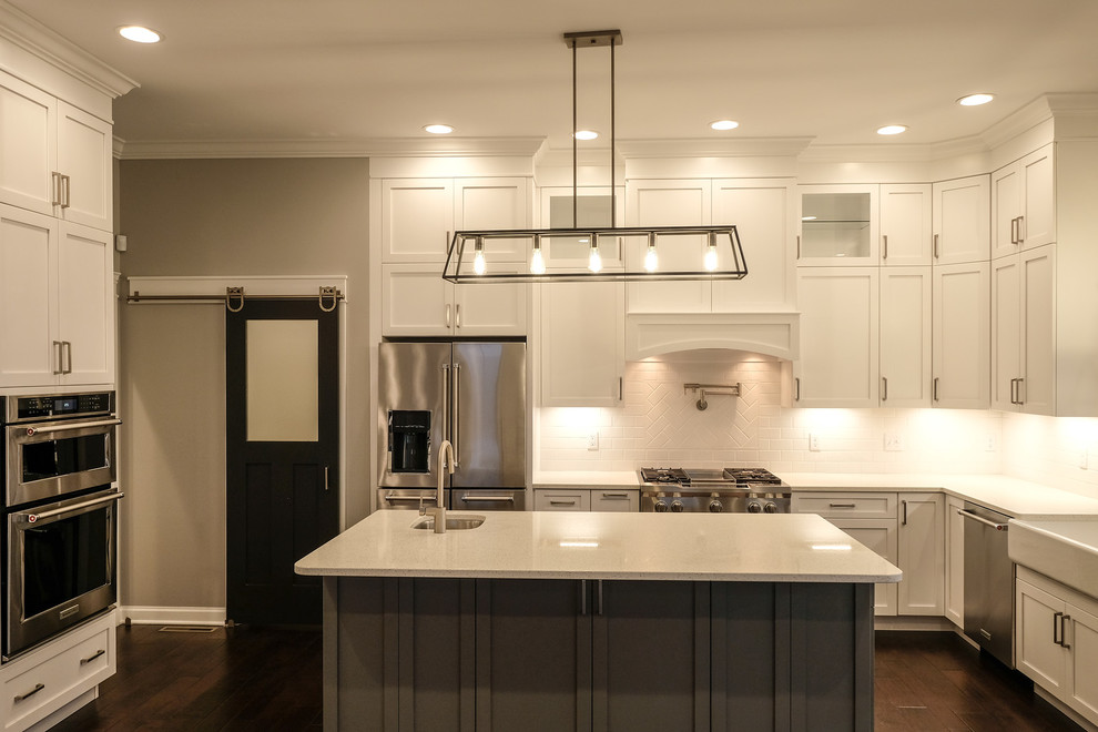 Large transitional u-shaped dark wood floor and brown floor eat-in kitchen photo with a farmhouse sink, recessed-panel cabinets, white cabinets, quartz countertops, white backsplash, stainless steel appliances, an island and white countertops