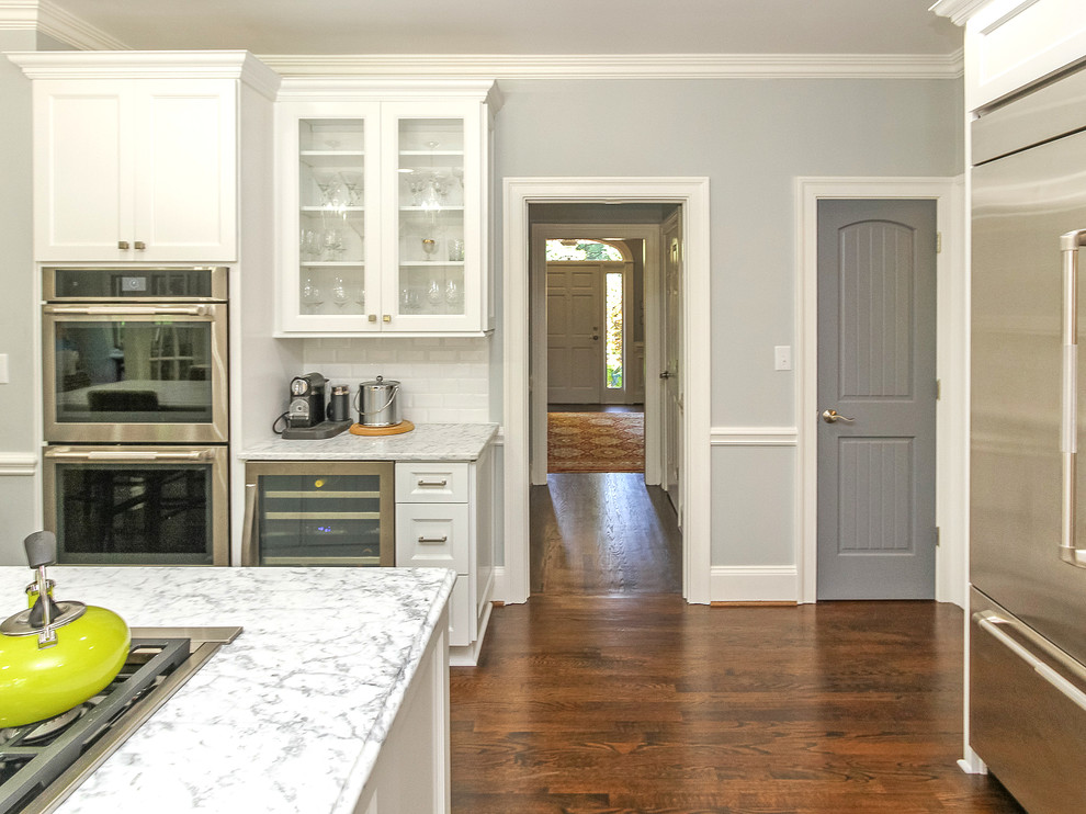 Inspiration for a mid-sized traditional galley eat-in kitchen in Charlotte with a farmhouse sink, shaker cabinets, white cabinets, quartz benchtops, white splashback, ceramic splashback, stainless steel appliances, dark hardwood floors, with island and brown floor.
