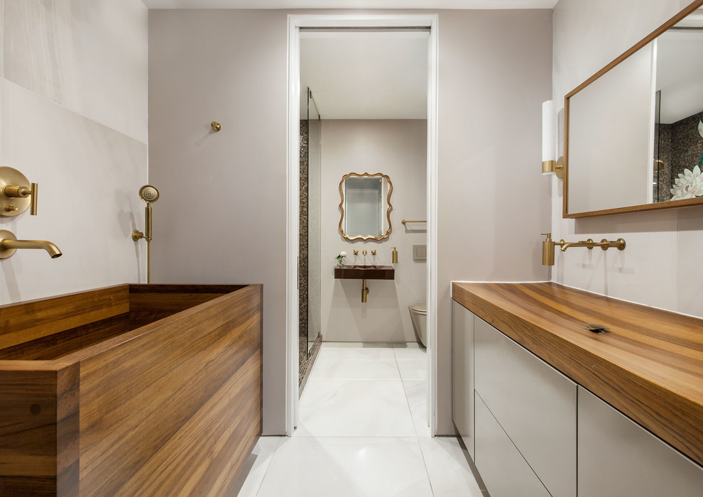 Mid-sized contemporary master bathroom in New York with flat-panel cabinets, beige cabinets, a japanese tub, a wall-mount toilet, beige tile, porcelain tile, beige walls, porcelain floors, a trough sink, wood benchtops, an open shower, an open shower and white floor.