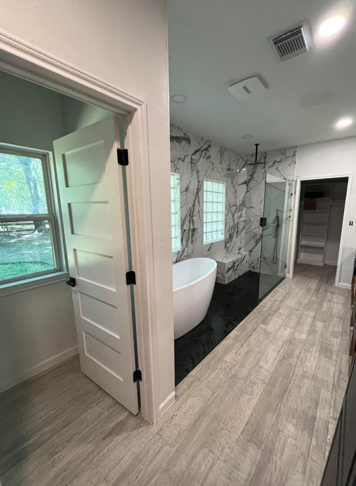 This is an example of a large master bathroom in Houston with black cabinets, a freestanding tub, a curbless shower, a two-piece toilet, black and white tile, porcelain tile, white walls, wood-look tile, an undermount sink, marble benchtops, grey floor, an open shower, white benchtops, a shower seat, a double vanity and a built-in vanity.