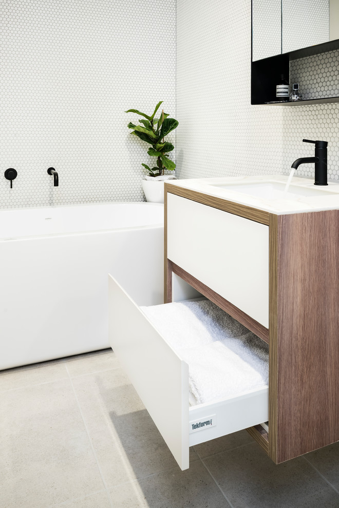 This is an example of a small contemporary bathroom in Melbourne with dark wood cabinets, a freestanding tub, white tile, white walls, an integrated sink, grey floor and white benchtops.