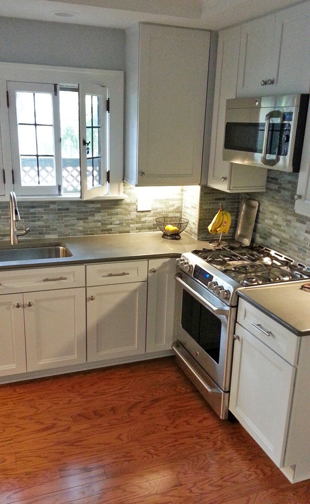 Enclosed kitchen - mid-sized transitional u-shaped dark wood floor and brown floor enclosed kitchen idea in Cleveland with an undermount sink, shaker cabinets, white cabinets, quartz countertops, gray backsplash, mosaic tile backsplash, stainless steel appliances, no island and gray countertops