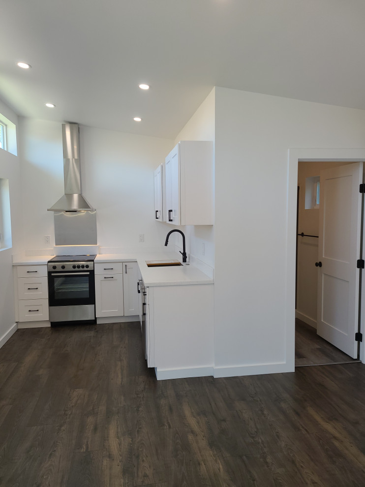 This is an example of a medium sized retro l-shaped open plan kitchen in Los Angeles with a single-bowl sink, raised-panel cabinets, white cabinets, composite countertops, stainless steel appliances, vinyl flooring, no island, brown floors and white worktops.
