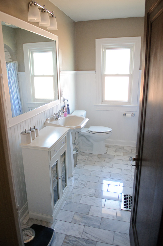 Small midcentury bathroom in Indianapolis with a pedestal sink, flat-panel cabinets, white cabinets, a drop-in tub, a shower/bathtub combo, white tile and marble floors.