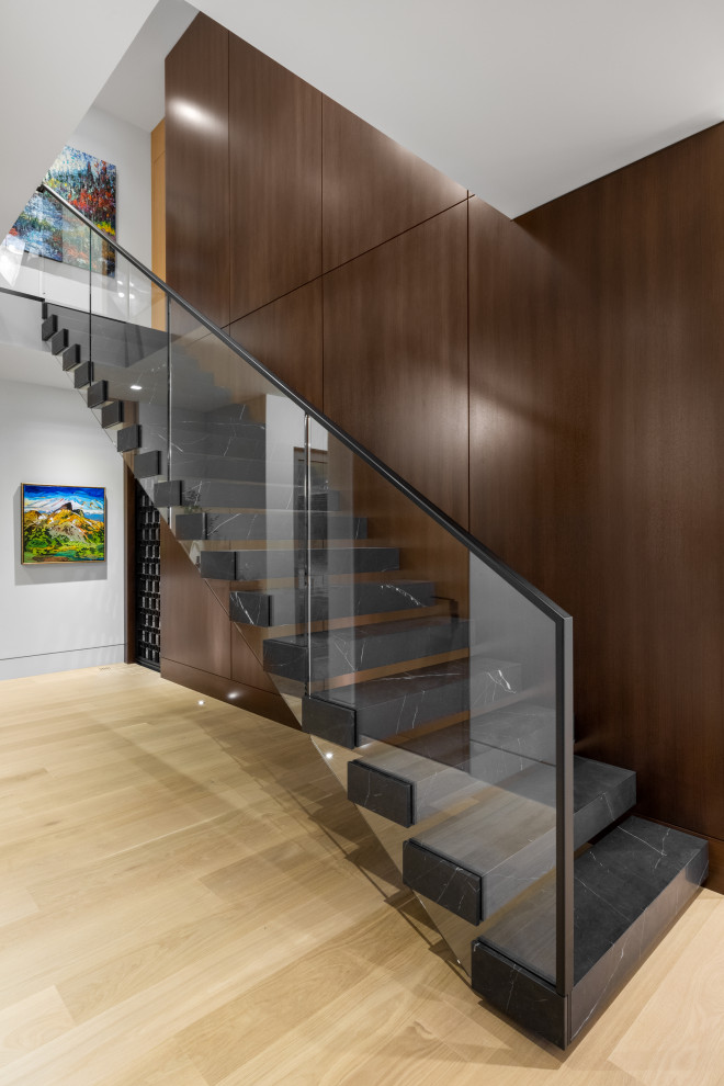 Diseño de escalera recta moderna de tamaño medio con escalones de mármol, contrahuellas de vidrio, barandilla de metal y panelado