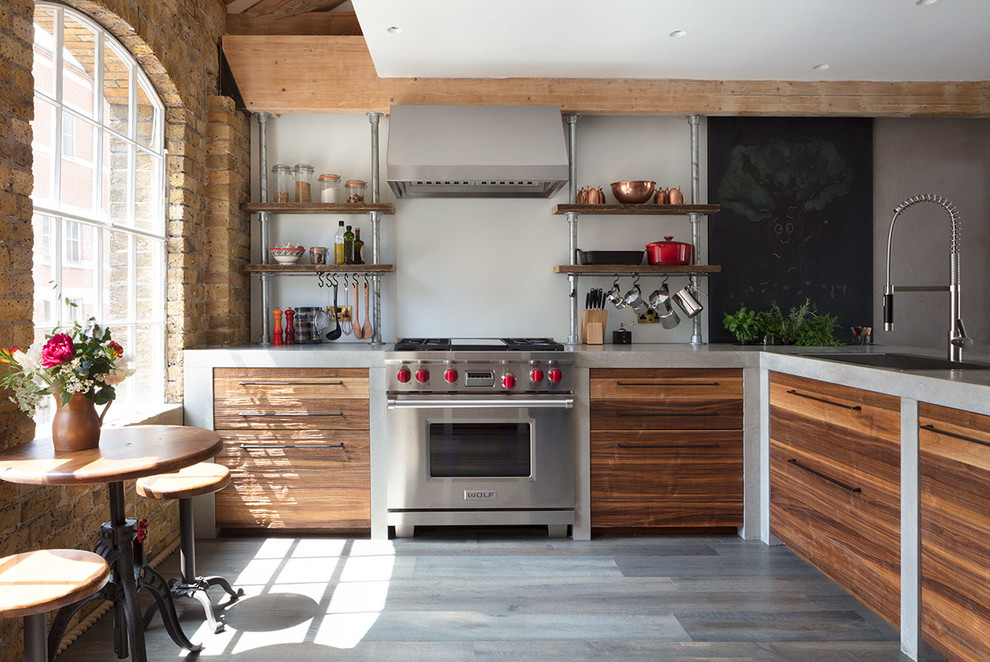 This is an example of a large industrial l-shaped open plan kitchen in London with an integrated sink, concrete benchtops, grey splashback, light hardwood floors, no island, grey floor, grey benchtop, flat-panel cabinets, stainless steel appliances and medium wood cabinets.