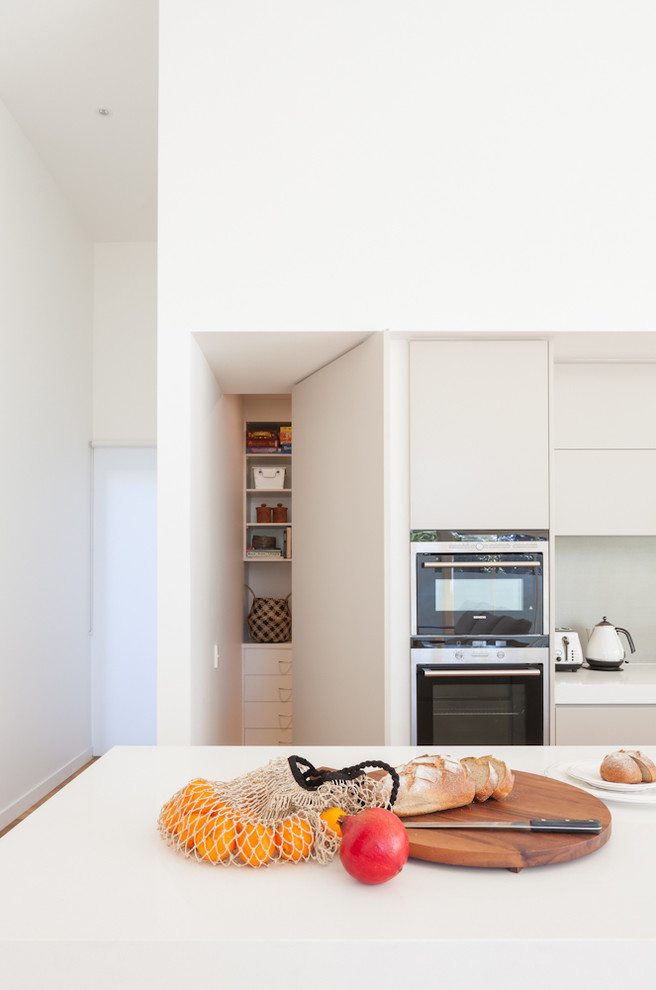 Inspiration for a mid-sized contemporary galley kitchen pantry in Sydney with an undermount sink, flat-panel cabinets, beige cabinets, solid surface benchtops, grey splashback, stainless steel appliances, medium hardwood floors, with island, brown floor and porcelain splashback.