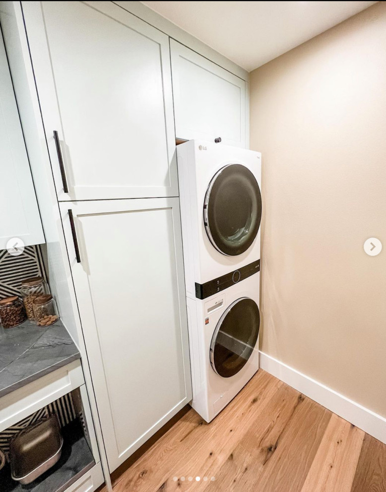 Design ideas for a small country galley dedicated laundry room in Seattle with an utility sink, recessed-panel cabinets, white cabinets, white splashback, porcelain splashback, beige walls, medium hardwood floors, a stacked washer and dryer and grey benchtop.