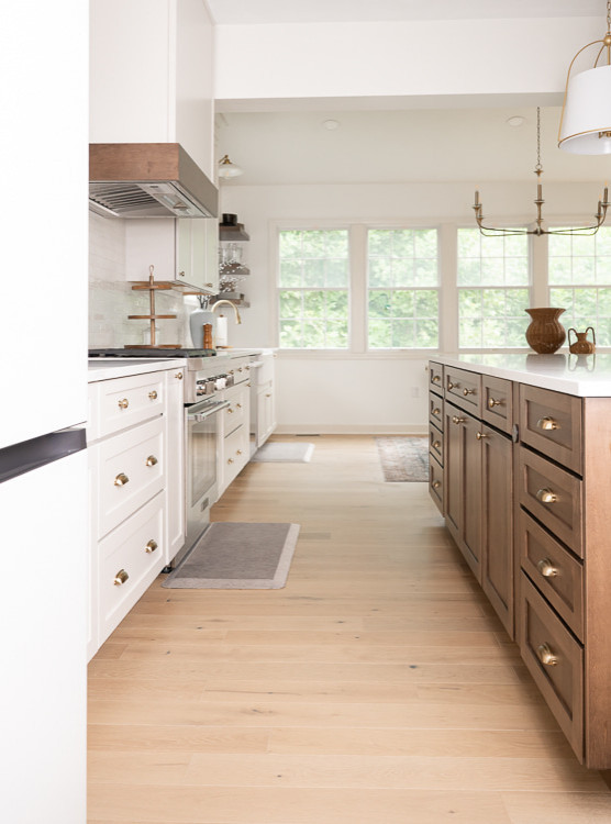 Large transitional u-shaped light wood floor, brown floor and vaulted ceiling eat-in kitchen photo with an undermount sink, shaker cabinets, white cabinets, quartz countertops, white backsplash, porcelain backsplash, stainless steel appliances, an island and white countertops