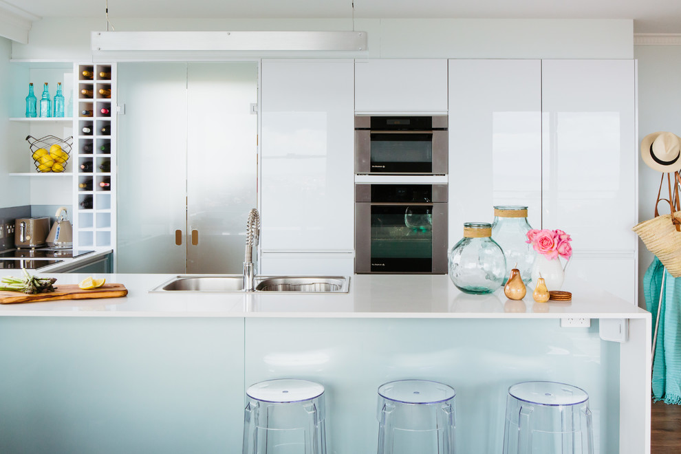 Small beach style u-shaped kitchen in Sydney with a double-bowl sink, granite benchtops, stainless steel appliances and light hardwood floors.