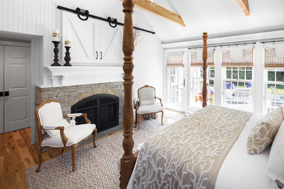 Inspiration for a large beach style master bedroom in Boston with white walls, a standard fireplace, a stone fireplace surround, dark hardwood floors and brown floor.