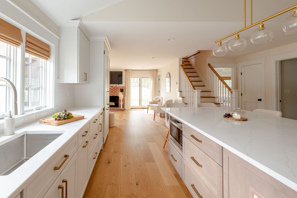 Eat-in kitchen - huge transitional l-shaped light wood floor, brown floor and vaulted ceiling eat-in kitchen idea in Boston with an undermount sink, shaker cabinets, white cabinets, quartz countertops, white backsplash, ceramic backsplash, paneled appliances, an island and white countertops