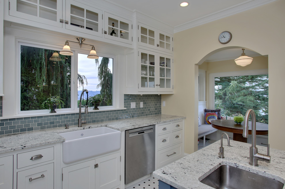 Photo of an arts and crafts eat-in kitchen in Seattle with a farmhouse sink, glass-front cabinets, white cabinets, granite benchtops, blue splashback, glass tile splashback, stainless steel appliances, ceramic floors and with island.
