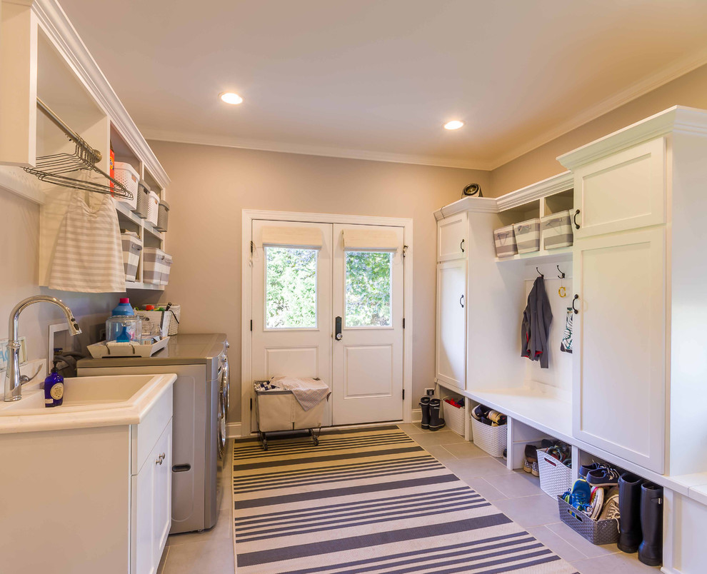 Mid-sized traditional galley dedicated laundry room in Chicago with an utility sink, shaker cabinets, white cabinets, solid surface benchtops, ceramic floors, a side-by-side washer and dryer, grey floor, beige walls, white benchtop, white splashback, cement tile splashback, wallpaper and wallpaper.