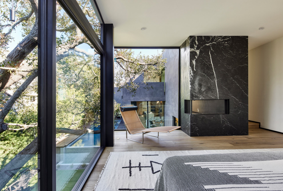 Großes Modernes Hauptschlafzimmer mit grauer Wandfarbe, hellem Holzboden, Eckkamin, Kaminumrandung aus Stein, beigem Boden und Wandgestaltungen in Los Angeles