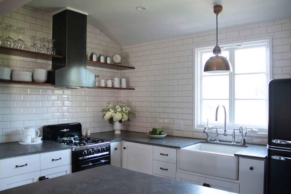 This is an example of a traditional l-shaped kitchen in Los Angeles with open cabinets, black appliances, a farmhouse sink, white splashback, subway tile splashback and limestone benchtops.