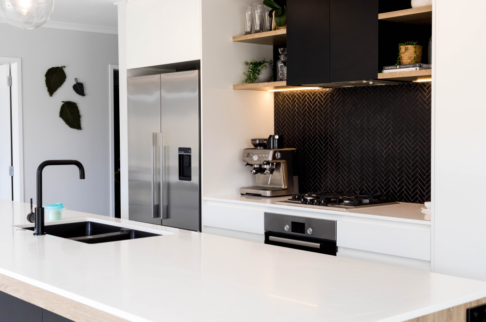 Mid-sized scandinavian galley eat-in kitchen in Auckland with a double-bowl sink, flat-panel cabinets, black cabinets, solid surface benchtops, black splashback, mosaic tile splashback, stainless steel appliances, porcelain floors, with island, grey floor and white benchtop.