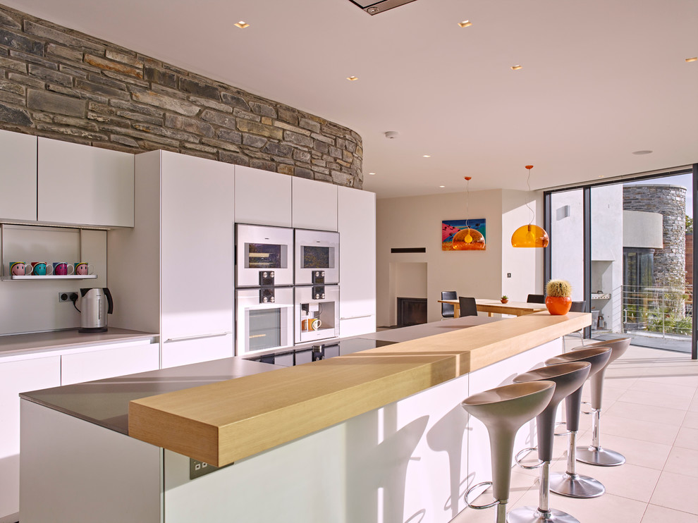 Mid-sized contemporary eat-in kitchen in Devon with flat-panel cabinets, white cabinets, solid surface benchtops, white splashback, ceramic floors, with island and white appliances.