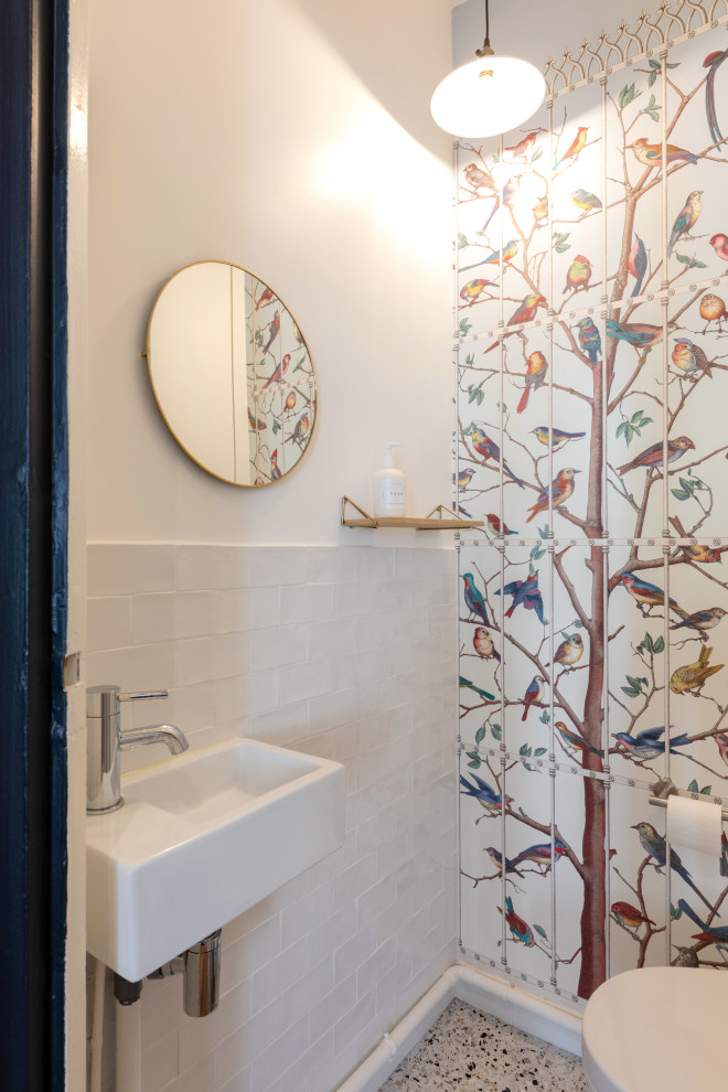 Photo of a small scandinavian powder room in Paris with open cabinets, white cabinets, a wall-mount toilet, white tile, terra-cotta tile, white walls, terrazzo floors, a wall-mount sink, solid surface benchtops, white floor, white benchtops, a freestanding vanity and wallpaper.
