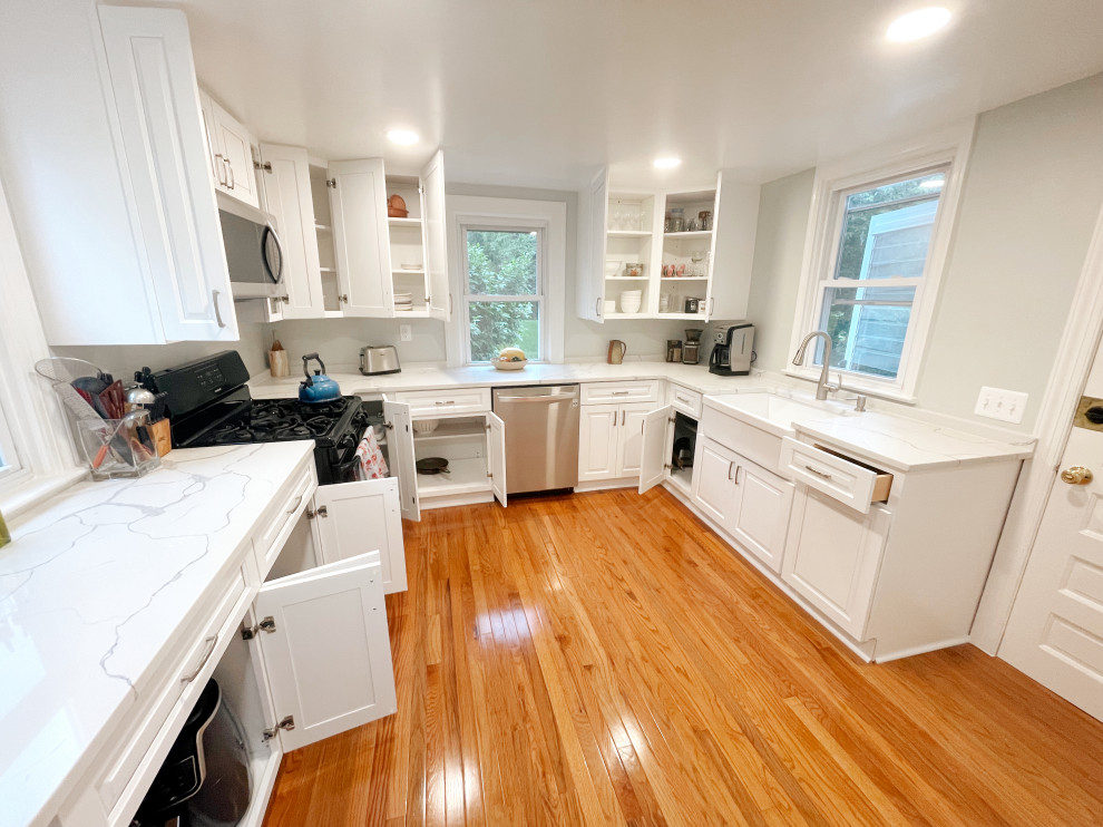 Photo of a mid-sized modern eat-in kitchen in DC Metro with a farmhouse sink, shaker cabinets, white cabinets, quartzite benchtops, white splashback, stainless steel appliances, light hardwood floors, brown floor and white benchtop.