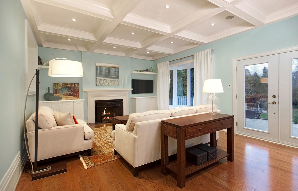 This is an example of a mid-sized traditional formal enclosed living room in Toronto with blue walls, medium hardwood floors, a standard fireplace, a wood fireplace surround, a wall-mounted tv and brown floor.