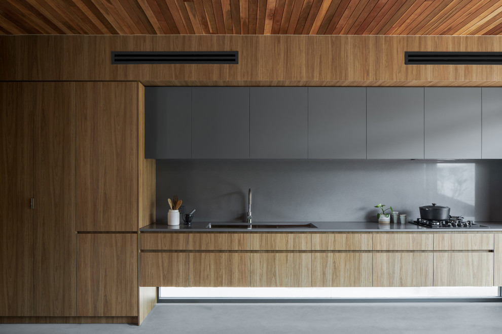 Zweizeilige Moderne Küche mit Unterbauwaschbecken, flächenbündigen Schrankfronten, hellen Holzschränken, Küchenrückwand in Grau, Elektrogeräten mit Frontblende, Kücheninsel, grauem Boden, grauer Arbeitsplatte und Holzdecke in Brisbane