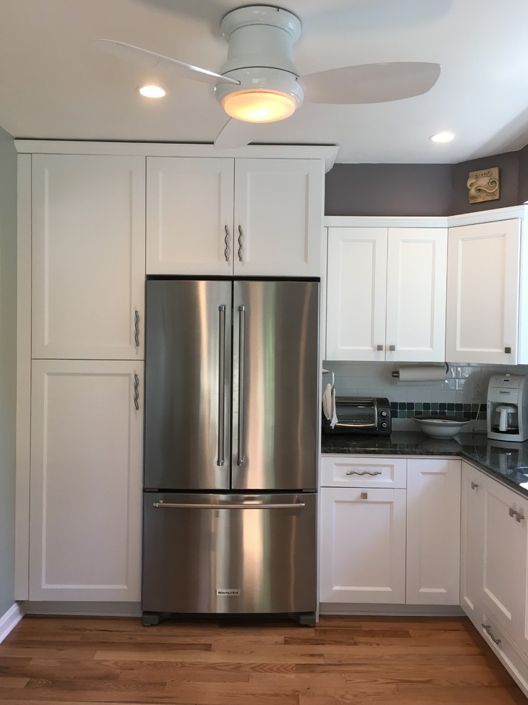 Mid-sized transitional l-shaped light wood floor enclosed kitchen photo with an undermount sink, flat-panel cabinets, white cabinets, granite countertops, white backsplash, subway tile backsplash, stainless steel appliances and no island
