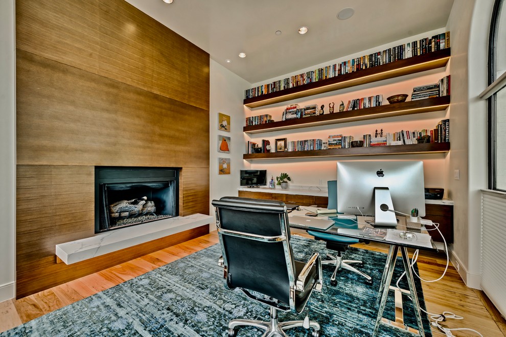 This is an example of a large transitional study room in Dallas with grey walls, medium hardwood floors, a ribbon fireplace, a wood fireplace surround and a freestanding desk.