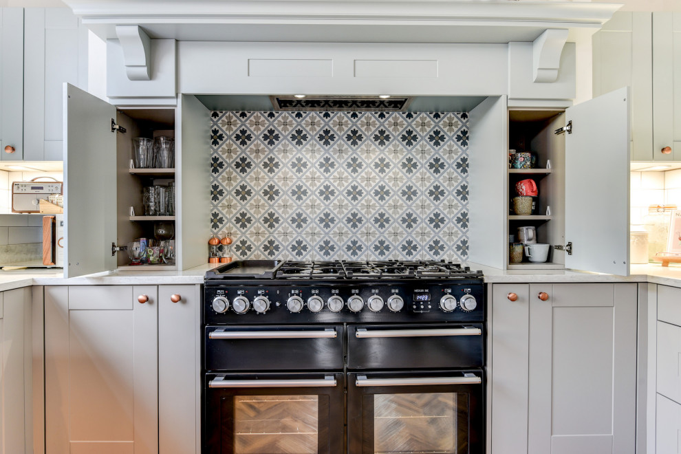 Inredning av ett klassiskt stort vit vitt kök, med en rustik diskho, skåp i shakerstil, blå skåp, bänkskiva i kvartsit, vitt stänkskydd, stänkskydd i tunnelbanekakel, svarta vitvaror, mellanmörkt trägolv, en halv köksö och brunt golv