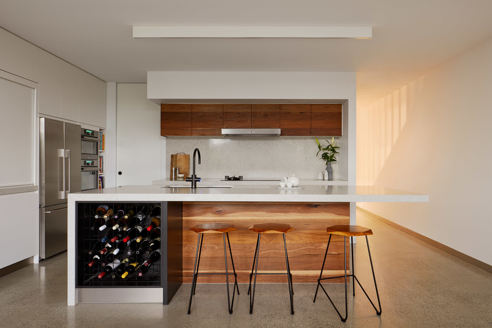 Photo of a mid-sized contemporary l-shaped open plan kitchen in Melbourne with an undermount sink, flat-panel cabinets, medium wood cabinets, solid surface benchtops, beige splashback, stainless steel appliances, concrete floors, with island, grey floor and stone slab splashback.