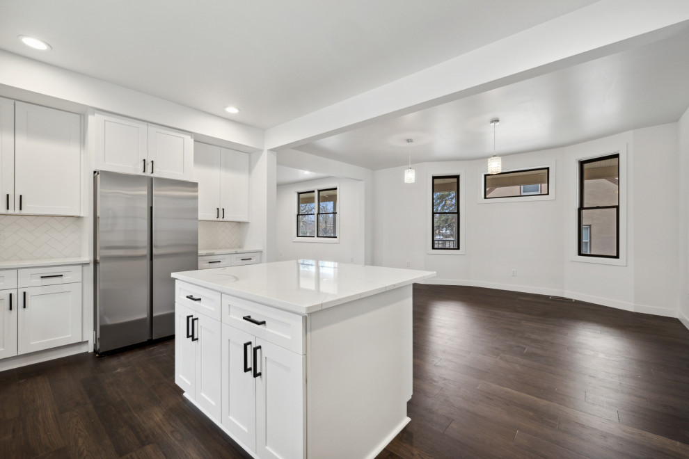 Inspiration for a large transitional u-shaped dark wood floor and brown floor eat-in kitchen remodel in Minneapolis with a single-bowl sink, shaker cabinets, white cabinets, quartz countertops, white backsplash, ceramic backsplash, stainless steel appliances, an island and white countertops