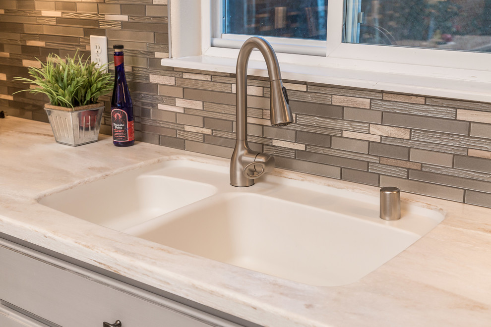 Mid-sized transitional l-shaped open concept kitchen photo with an undermount sink, raised-panel cabinets, gray cabinets, solid surface countertops, metallic backsplash, mosaic tile backsplash, stainless steel appliances and an island