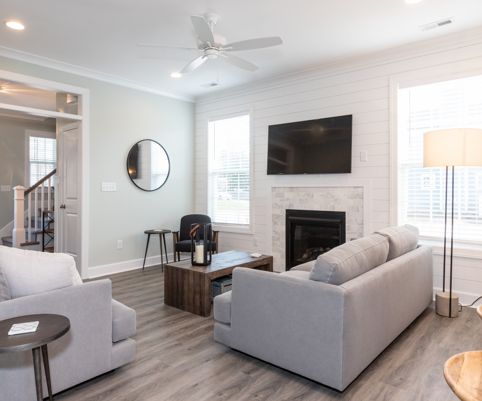Photo of a mid-sized beach style open concept family room in Other with laminate floors, a standard fireplace, a tile fireplace surround, a wall-mounted tv, grey floor and grey walls.