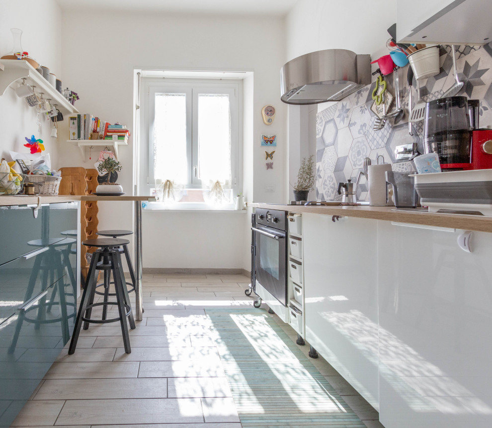 Eclectic galley kitchen in Rome with flat-panel cabinets, white cabinets, wood benchtops, grey splashback, black appliances, beige floor and beige benchtop.