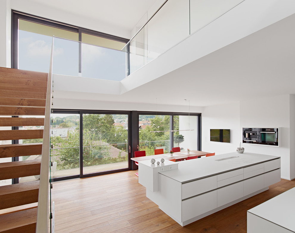 This is an example of a large contemporary open plan kitchen in Stuttgart with with island, flat-panel cabinets, white cabinets, black appliances and medium hardwood floors.