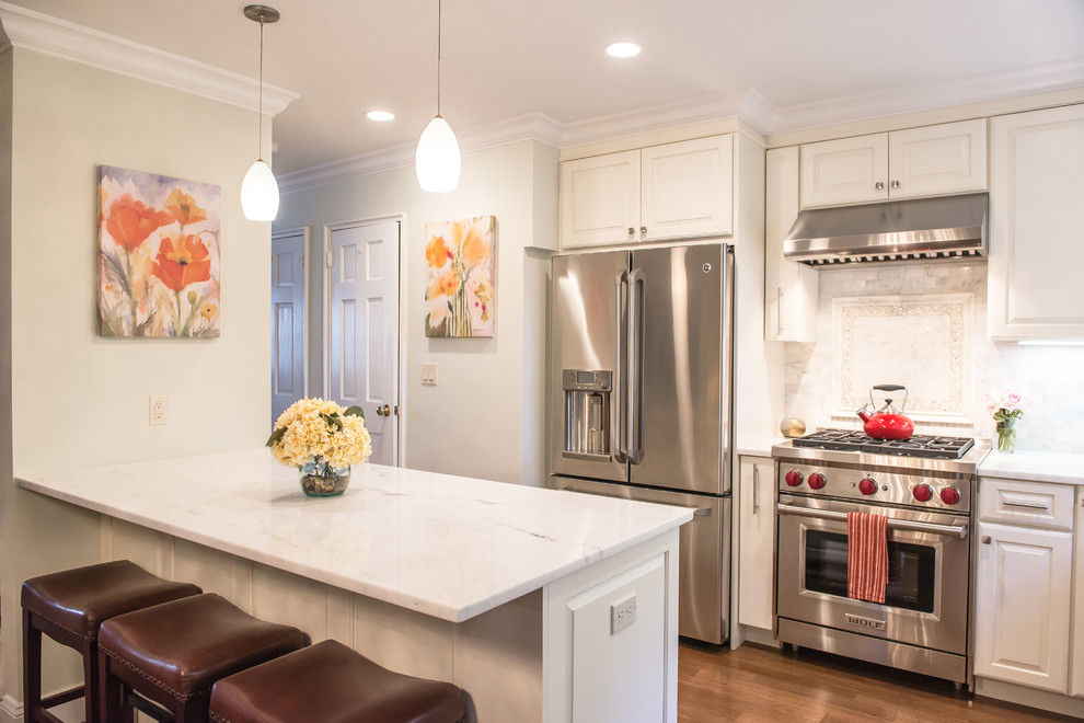 Photo of a mid-sized traditional l-shaped eat-in kitchen in New York with raised-panel cabinets, white cabinets, white splashback, stainless steel appliances, medium hardwood floors, a peninsula, an undermount sink, marble benchtops and stone tile splashback.