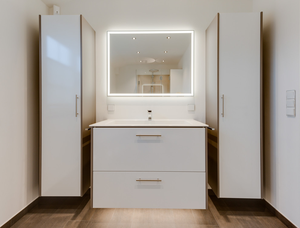 This is an example of a large contemporary 3/4 bathroom in Hamburg with flat-panel cabinets, white cabinets, a corner tub, a corner shower, a wall-mount toilet, beige tile, ceramic tile, white walls, light hardwood floors, a drop-in sink, solid surface benchtops, beige floor and a hinged shower door.