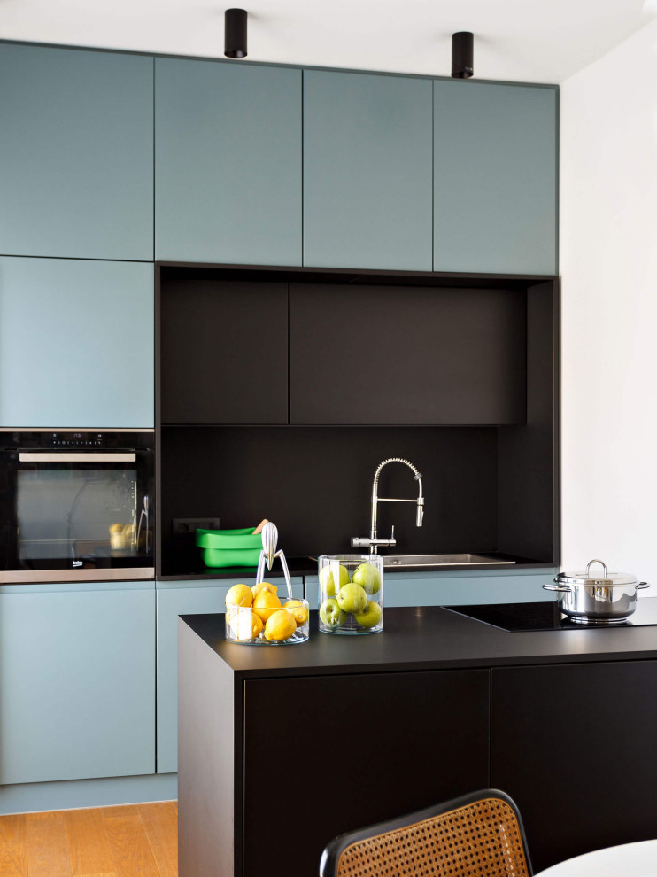 This is an example of a mid-sized contemporary single-wall open plan kitchen in Rome with a drop-in sink, beaded inset cabinets, turquoise cabinets, stainless steel appliances, with island and black benchtop.