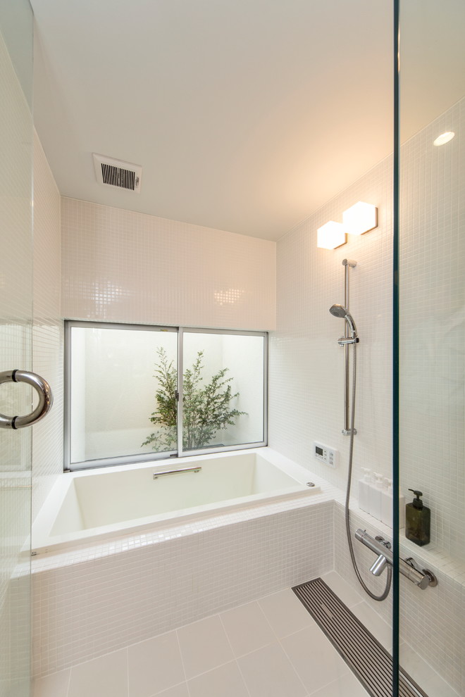 This is an example of a small modern master bathroom in Nagoya with a drop-in tub, white tile, white walls and a hinged shower door.