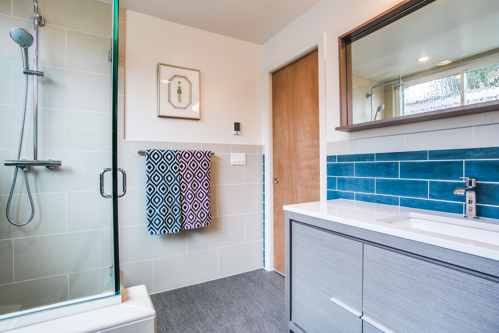 This is an example of a small midcentury master bathroom in Seattle with furniture-like cabinets, grey cabinets, a corner shower, a two-piece toilet, blue tile, ceramic tile, beige walls, laminate floors, an undermount sink, engineered quartz benchtops, grey floor and a hinged shower door.