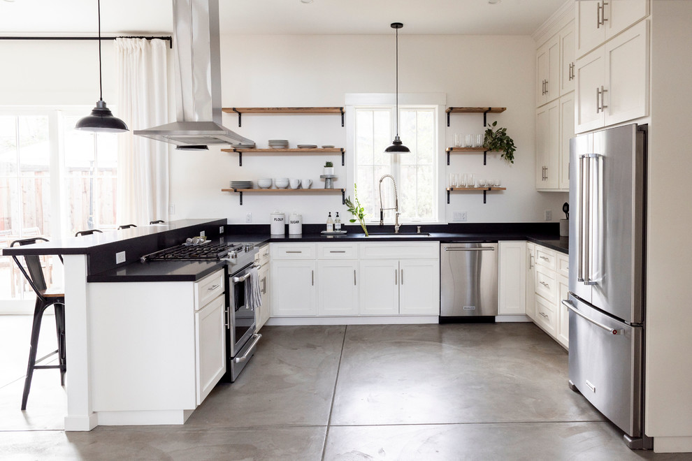 This is an example of a mid-sized country u-shaped separate kitchen in San Francisco with a drop-in sink, white cabinets, quartzite benchtops, black splashback, stainless steel appliances, cement tiles, grey floor and black benchtop.