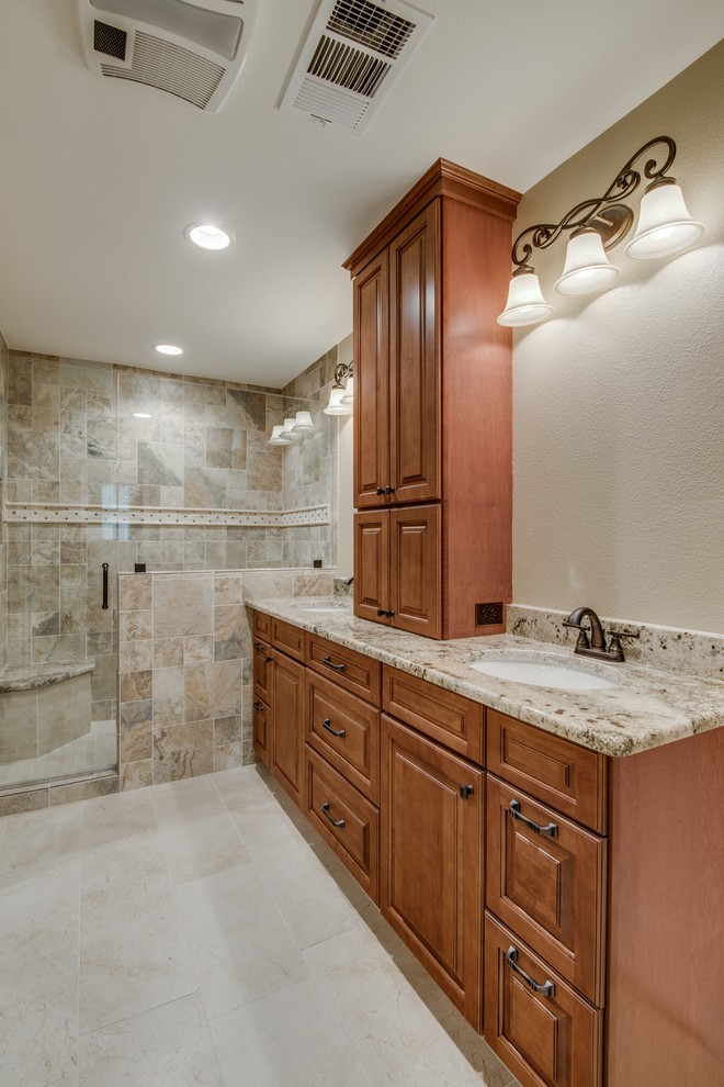 Design ideas for a mid-sized traditional master bathroom in Austin with shaker cabinets, brown cabinets, an alcove shower, a one-piece toilet, beige tile, porcelain tile, beige walls, ceramic floors, a drop-in sink, granite benchtops, beige floor, a hinged shower door and beige benchtops.