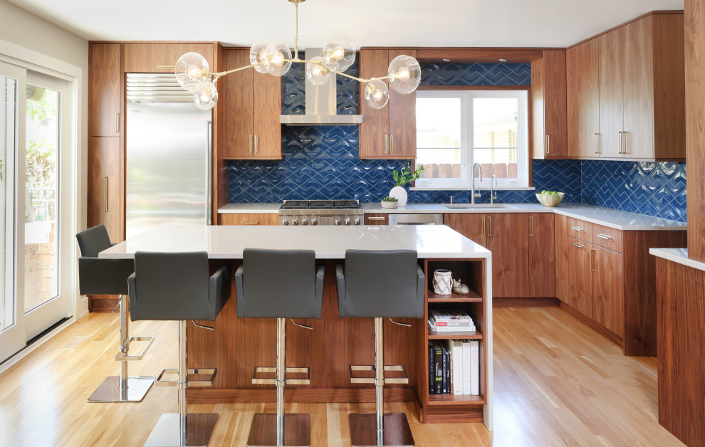 Photo of a mid-sized midcentury l-shaped eat-in kitchen in Chicago with a single-bowl sink, flat-panel cabinets, medium wood cabinets, quartzite benchtops, blue splashback, ceramic splashback, stainless steel appliances, light hardwood floors, with island, beige floor and white benchtop.