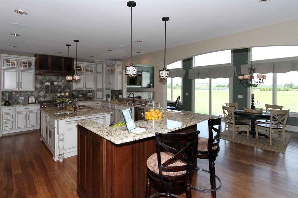 Large transitional u-shaped medium tone wood floor eat-in kitchen photo in Chicago with a double-bowl sink, raised-panel cabinets, white cabinets, granite countertops, brown backsplash, ceramic backsplash, stainless steel appliances and two islands