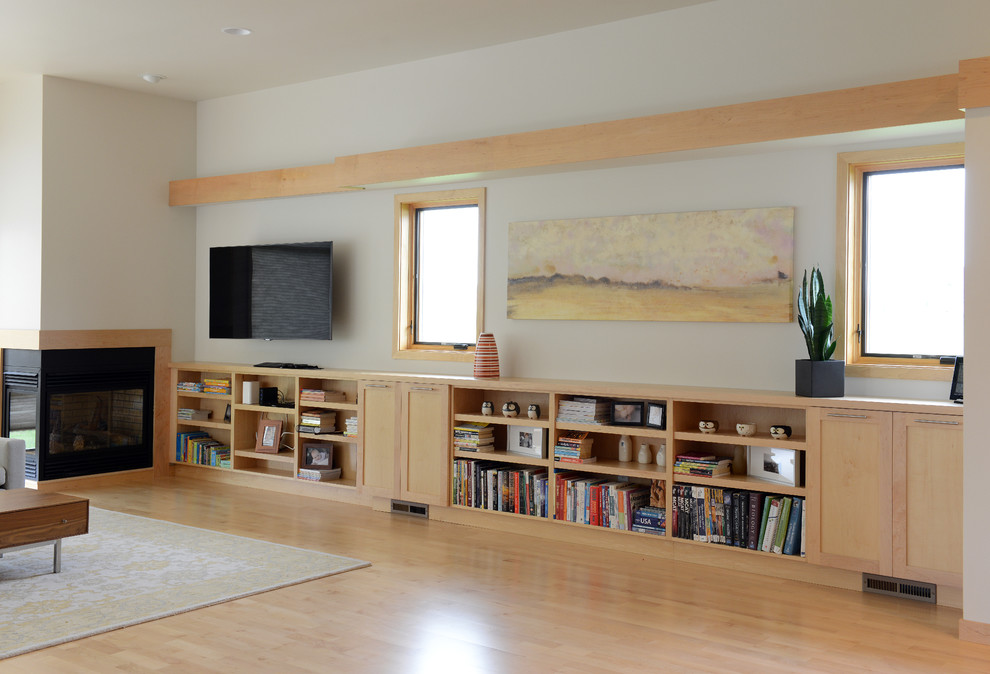 Photo of a contemporary open concept living room in Other with beige walls, light hardwood floors, a two-sided fireplace and a wall-mounted tv.