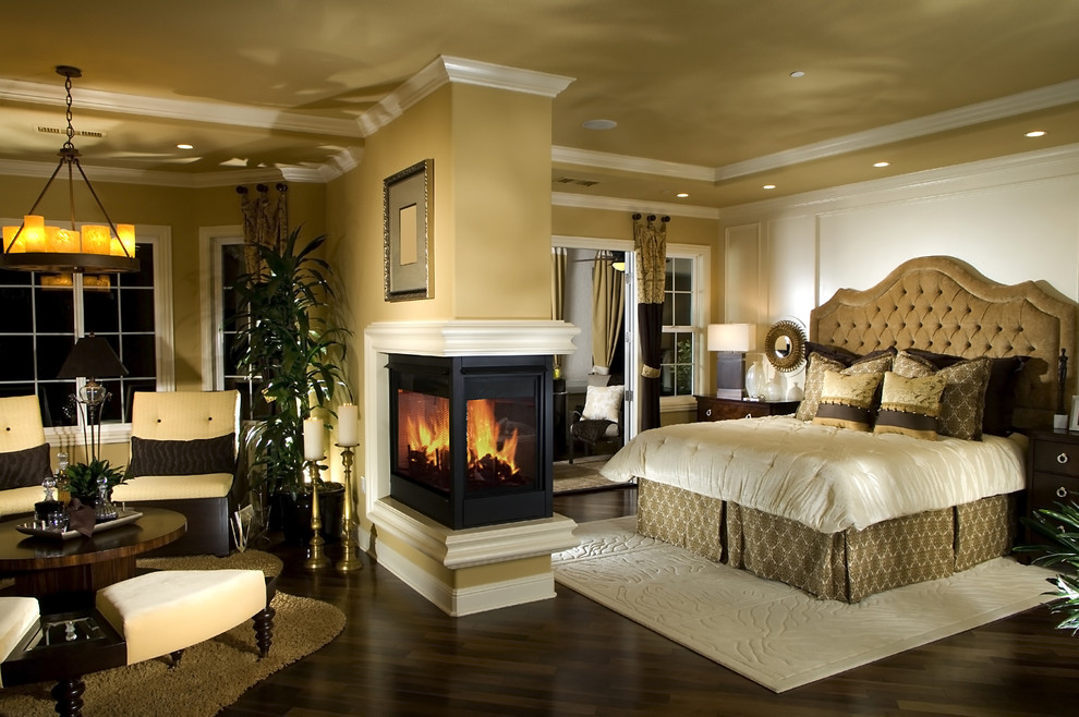 Design ideas for an expansive traditional master bedroom in Orange County with beige walls, dark hardwood floors, a two-sided fireplace and a wood fireplace surround.