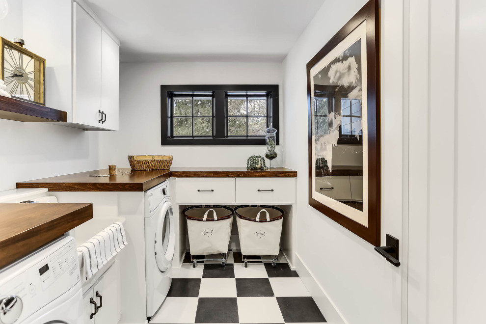 Inspiration for a transitional l-shaped laundry room in Minneapolis with an utility sink, flat-panel cabinets, white cabinets, wood benchtops, white walls, multi-coloured floor and brown benchtop.