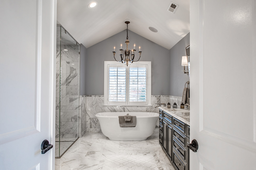 Inspiration for a large transitional master bathroom in Denver with raised-panel cabinets, grey cabinets, a freestanding tub, a curbless shower, a one-piece toilet, white tile, stone tile, grey walls, marble floors, an undermount sink and marble benchtops.